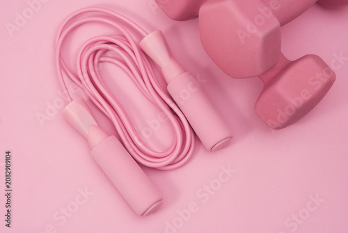 Top view pink dumbbells and jump rope on feminine fitness background