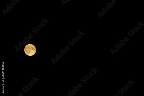 Small full moon on left side of black night sky with copy space