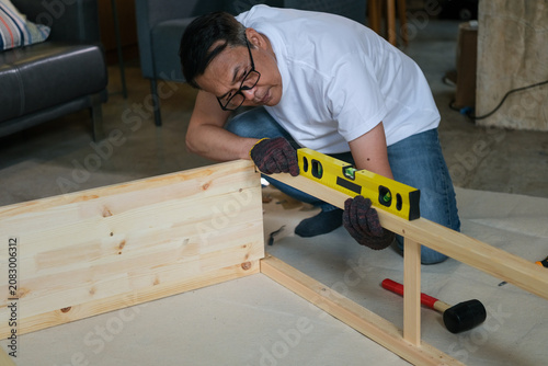Man, carpentry, wood, level, glove, home workshop, focused worker measuring pine frame during furniture assembly on floor