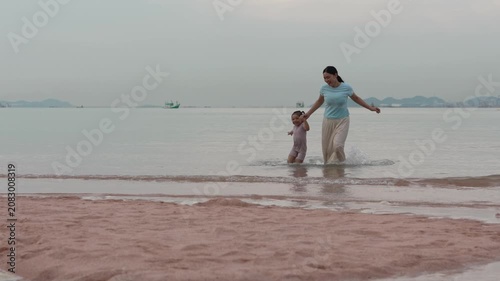 slow motion of happy preschool child girl running with mother on the sea beach in Pattaya, Thailand
