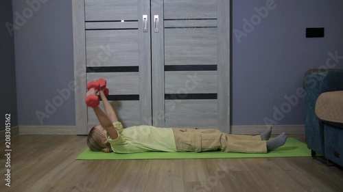 Young girl performing dumbbell exercises on yoga mat at home, engaging in fitness routine for upper body strength and physical well-being indoors.
