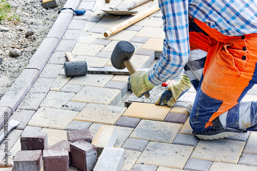 Worker lays down paving stones at a construction site in the afternoon, using a rubber mallet to ensure a strong fit