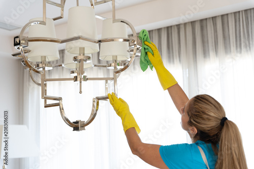 Foto Woman cleaning modern chandelier in a bright minimalist interior