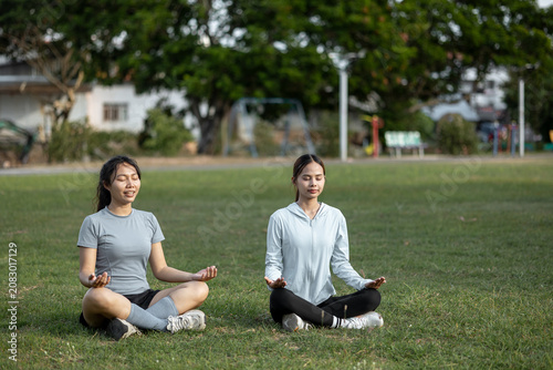 Two Young Women Meditating Together in Lotus Pose at a Park for Mindfulness, Mental Wellness and Healthy Lifestyle