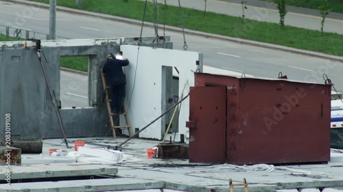 Welder On Ladder Joins Concrete Panels. Industrial Worker Uses Welding Machine On Site.