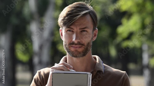 Handsome bearded man writing in notebook against beautiful green park background.