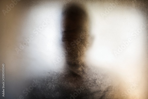 Silhouette of a mysterious person behind a frosted glass with textured blur