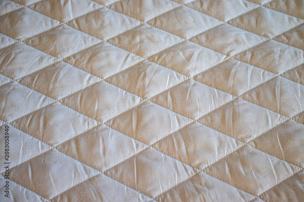 Fototapeta premium Beige quilted fabric texture with a geometric diamond pattern. Ideal backdrop for bedding catalogs, home textile website banners, or mattress manufacturing blogs.