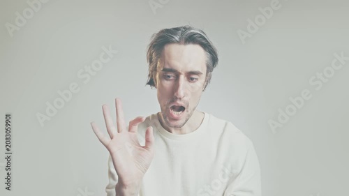 Young adult man making OK hand gesture, close-up portrait in white sweater against light gray background, multiple facial expressions, communication concept