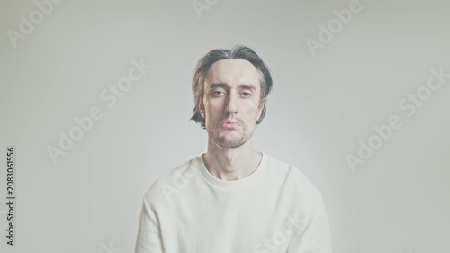 Young adult man sitting against plain light background with subtle sad or disappointed expression, straight-on portrait, soft lighting, shallow depth of field