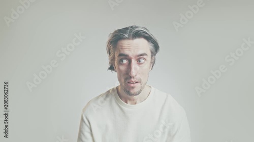 Surprised young man with wide-eyed expression sitting against neutral studio background, wearing light long-sleeve shirt, soft lighting, copy space, portrait