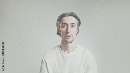 Surprised adult man making shocked and curious facial expressions in minimalist studio, soft lighting, light gray background, centered portrait with copy space