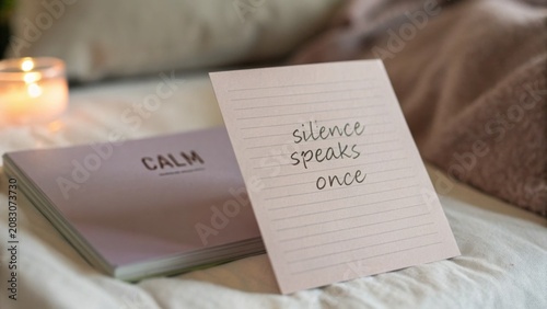 Inspirational quote card with message 'silence speaks once' on cozy bed with candle and soft textures for relaxation