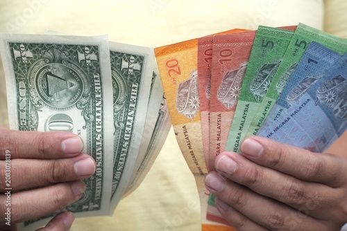 Canvastavla Close-up of hands holding Malaysian ringgit and US dollar banknotes, showing currency exchange, travel finance, and money comparison