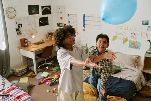 High angle shot of two boys playing with balloon in bedroom, moving actively and bonding through indoor fun. Suitable for family lifestyle, childhood, sibling, home activity campaigns