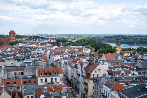 Foto Expansive cityscape (Torun, Poland) view over traditional red roofs and a medieval brick church, looking toward a river  Vistula with distant bridges