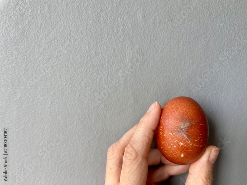 Close-up photograph of a fresh brown chicken egg with a feather attached to the shell, held in a hand against a neutral grey background. Natural farm-to-table concept representing fresh produce, 
