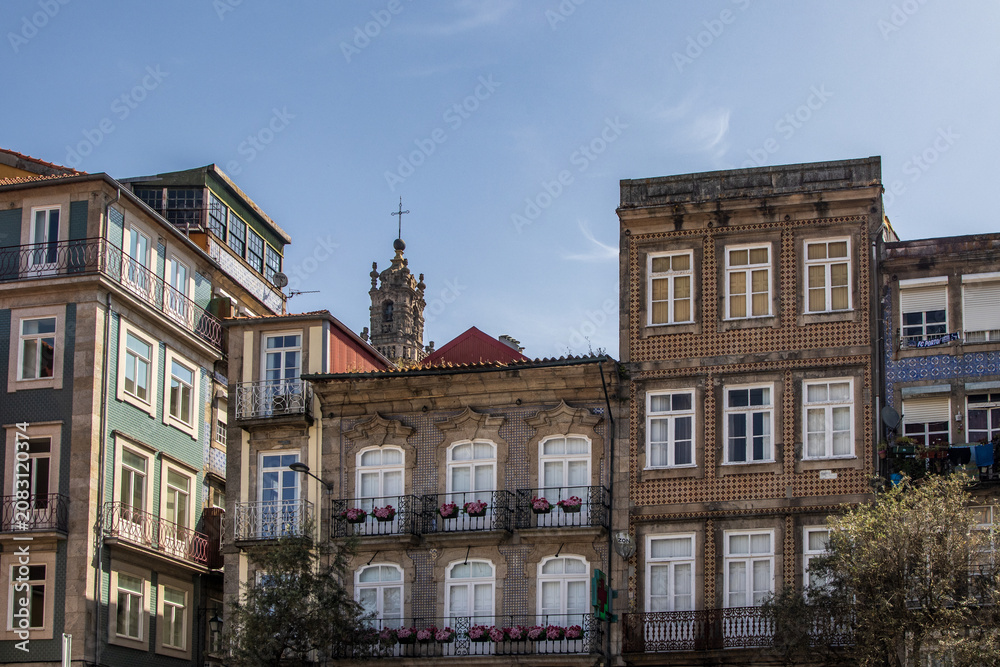 Obraz premium Vista frontal de hermosas fachadas históricas decoradas con azulejos típicos, balcones con flores y ventanas clásicas, con la Torre de los Clérigos asomando al fondo bajo un cielo despejado en Portuga