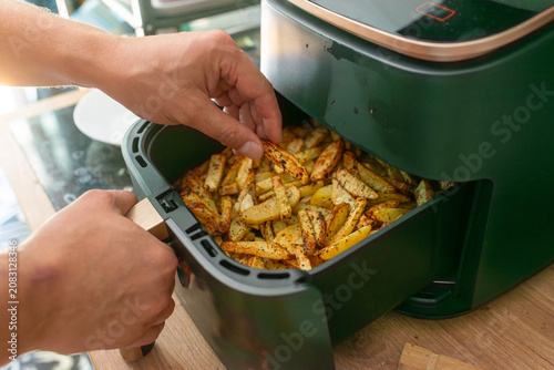 Close-up of hands opening an air fryer basket and checking golden potato fries cooked with herbs. Useful for homemade fast food, kitchen appliance use, healthy frying, meal preparation, and home cooki