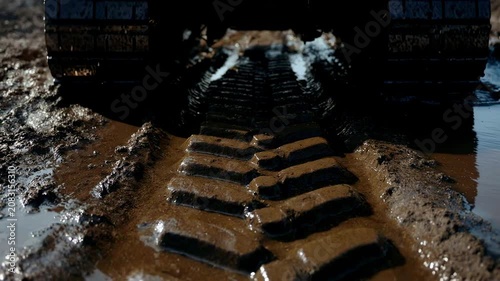 Close-up of heavy machinery tracks driving through thick mud. Crawler excavator leaving deep marks in wet dirt. Off-road construction equipment in action
