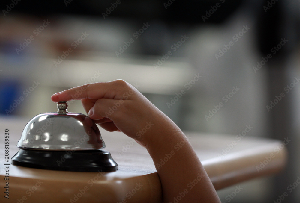 Naklejka premium Close-up of a kid ringing a chrome reception bell call button for attention or service with blurred background.