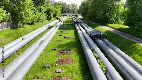 Aerial view of interconnected industrial pipes with green grass and walkways visible, showcasing the complex layout of a facility's piping system in an industrial setting