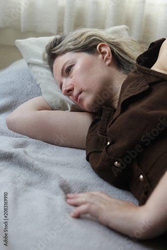 Photos Middle aged woman lying on a bed in an emotionally withdrawn pose with a depressed expression