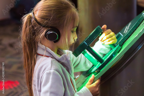 Canvas Print Child with long hair wearing headphones interacts with a green scientific displa