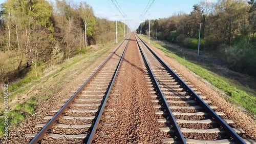 Train tracks stretch into the distance through a lush green landscape, showcasing the gradual transition of scenery along the railway corridor under a clear blue sky