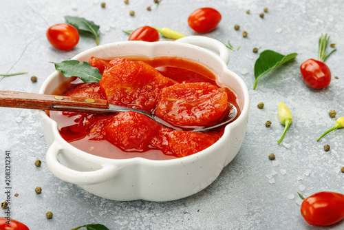 Canned whole peeled tomatoes in tomato juice in a white ceramic bowl with spoon. Rustic food styling