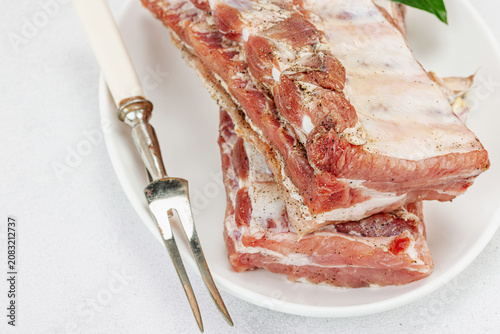 Raw pork ribs with garlic, spices and bay leaves on a white ceramic plate with a meat fork