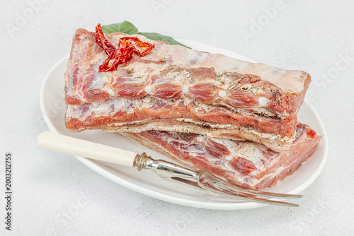 Raw pork ribs with garlic, spices and bay leaves on a white ceramic plate with a meat fork