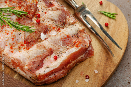 Raw marinated pork ribs with rosemary, spices and garlic on a wooden cutting board with a meat fork