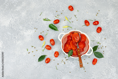 Canned whole peeled tomatoes in tomato juice in a white ceramic bowl with spoon. Rustic food styling
