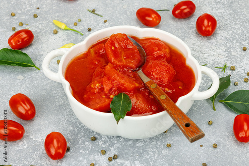 Canned whole peeled tomatoes in tomato juice in a white ceramic bowl with spoon. Rustic food styling