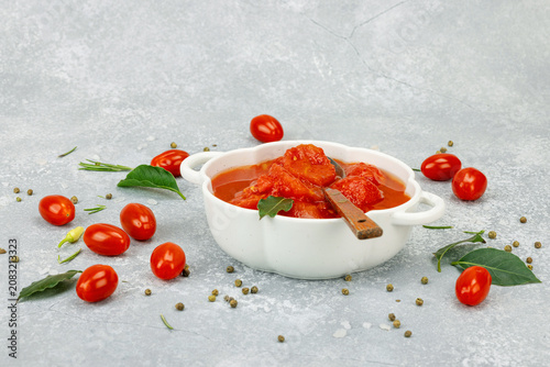 Canned whole peeled tomatoes in tomato juice in a white ceramic bowl with spoon. Rustic food styling