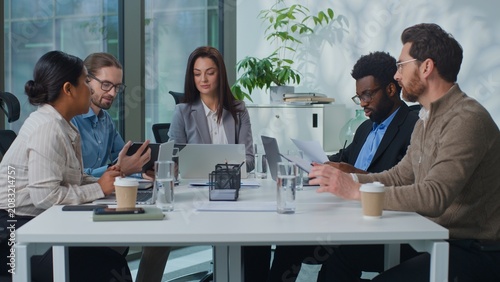 Multiracial business team executives gathering at conference table discussing data financial stats analyzing papers with laptop. Multiethnic workers reviewing chart discuss work collaborate at meeting