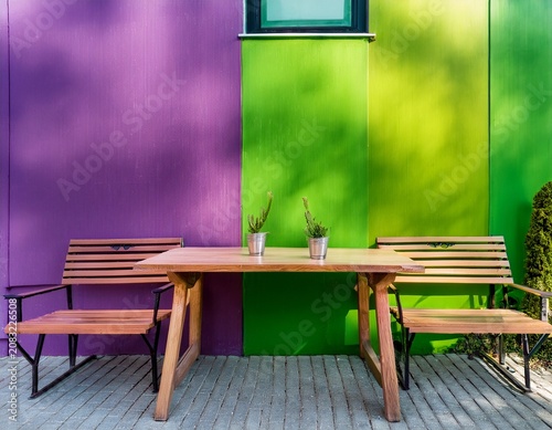 vibrant outdoor cafe seating area with a table and wooden benches against a bright purple and green wall
