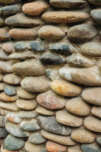 Background with the texture of a stone wall made of pebbles. Natural smooth pebbly stones. Finishing the facade of the building.