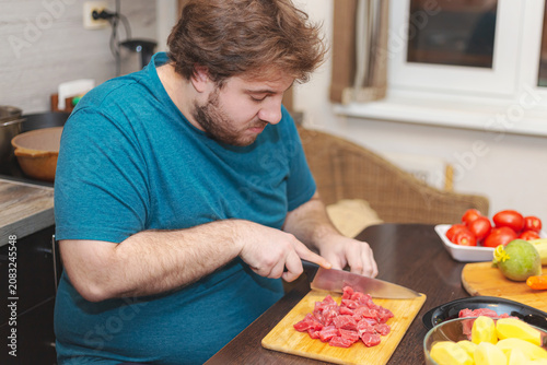 A young bearded Caucasian man cuts meat for lunch.