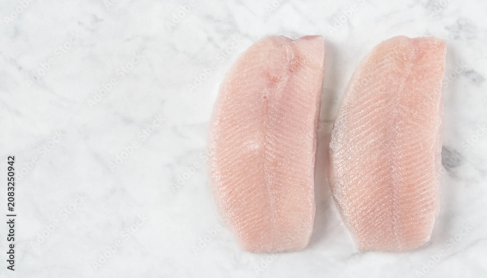 Fototapeta premium Two Raw Corvina Fillets on White Marble Surface