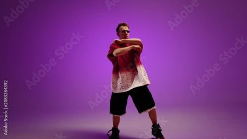 Hip hop dancer posing with sharp movement in a purple studio