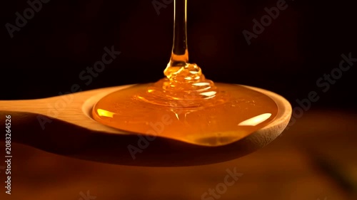 Golden Honey Dripping into a Wooden Spoon with Dark Background.