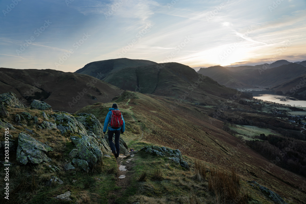 Obraz premium A female hiker walking over Rannerdale Knotts, Low Bank at dawn on a winters day in the Lake District, Cumbria, England, UK.