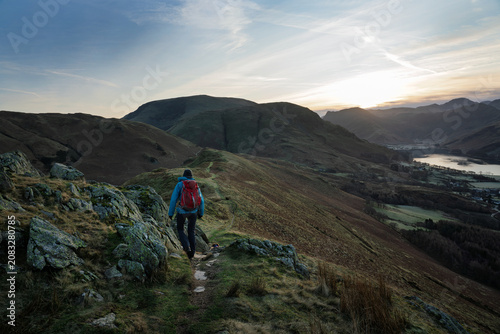 A female hiker walking over Rannerdale Knotts, Low Bank at dawn on a winters day in the Lake District, Cumbria, England, UK.