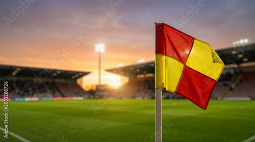 Close-up of a red and yellow corner flag on a stadium grass pitch at sunset