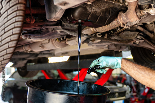 Bild auf Leinwand Mechanic performing an engine oil change while used motor oil drains from the oi