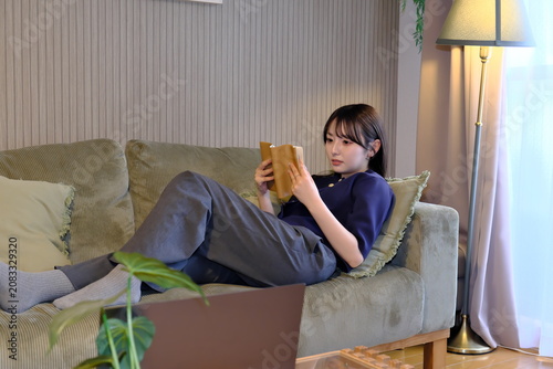 Photography 癒しの「自分時間」。ソファで寝ころびながら読書に没頭する女性の穏やかなライフスタイルシーン