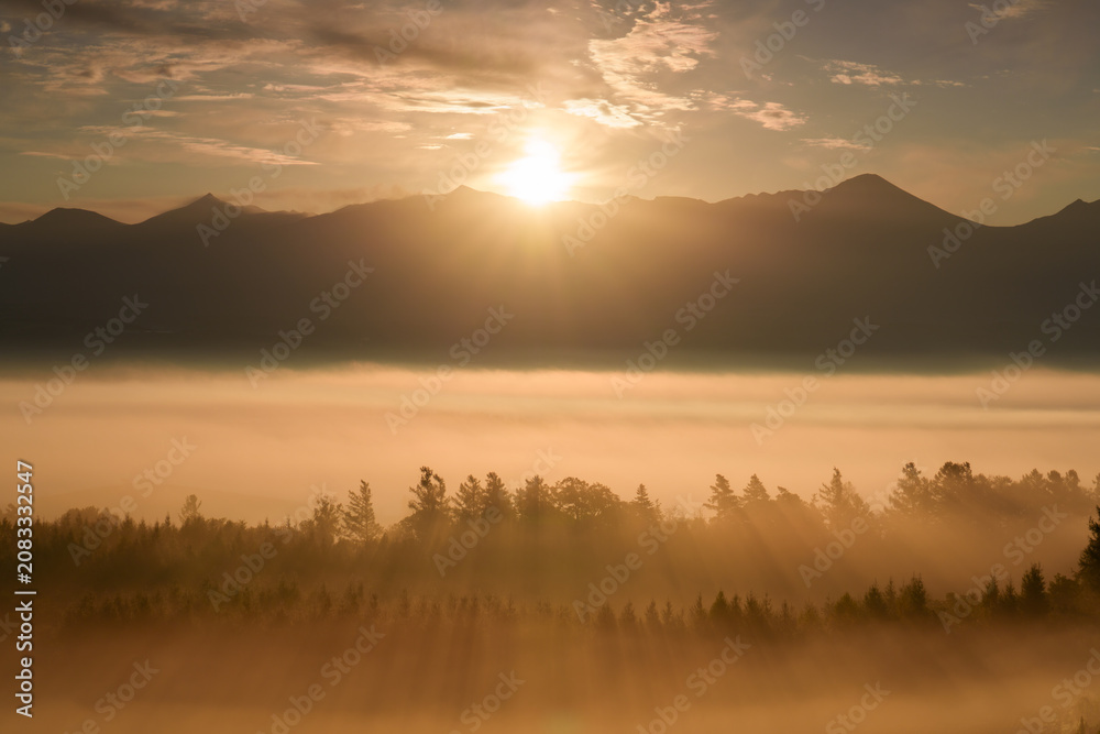 Obraz premium Sunrise over the Tokachi mountain range and sea of clouds from Senbo Pass in Kamifurano, Hokkaido, Japan