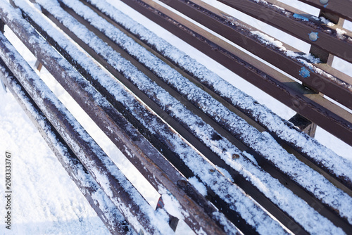 Snow accumulates on a bench made of wood and metal, showing a winter scene with no people around